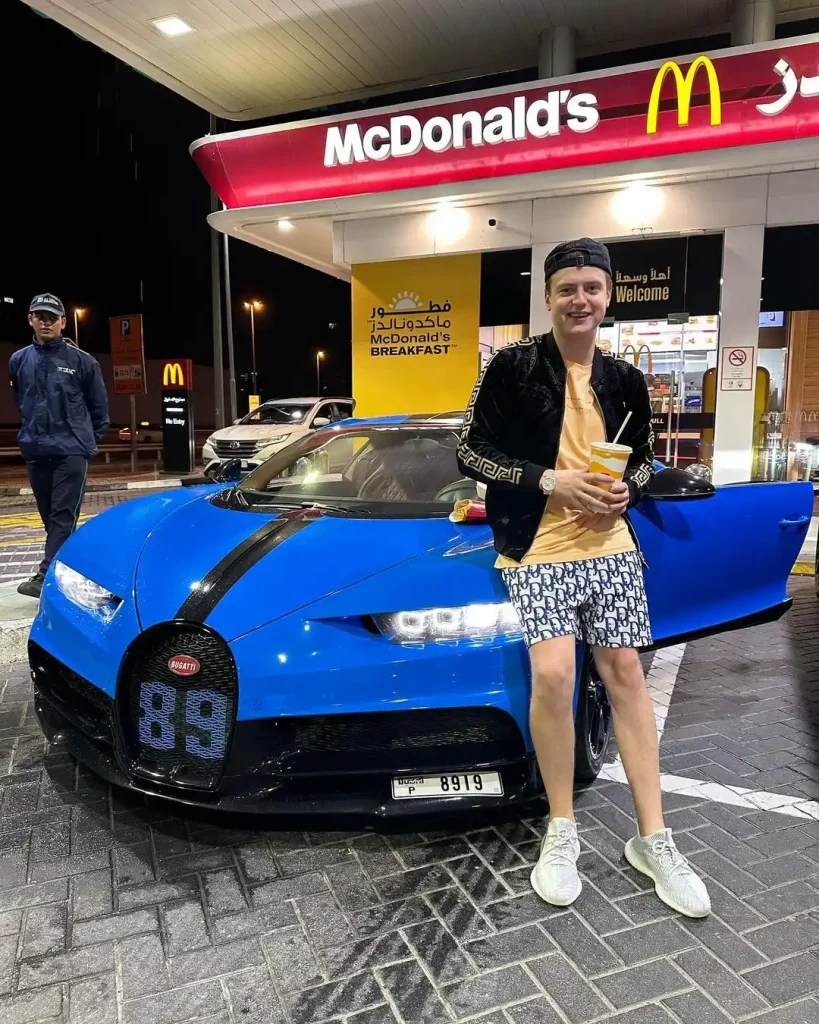 Mellstroy de pie junto a un coche deportivo azul fuera de una sala de exposiciones